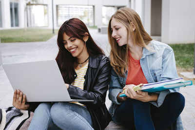 Young woman using mobile phone while sitting on laptop