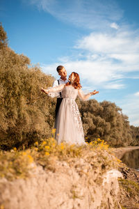 A young wedding couple in love on the edge of a cliff against the backdrop of the river and the sky.