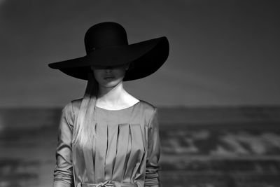 Woman wearing hat standing at beach against sky