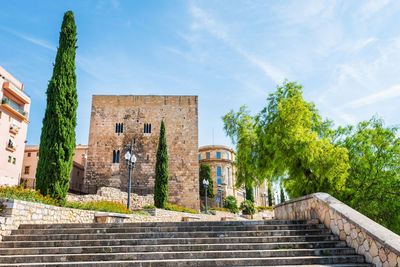 Low angle view of stone stairs and tower against a blue sky  in the old town of tarragona.