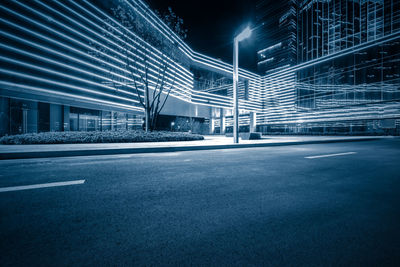 Empty road by illuminated buildings in city at night