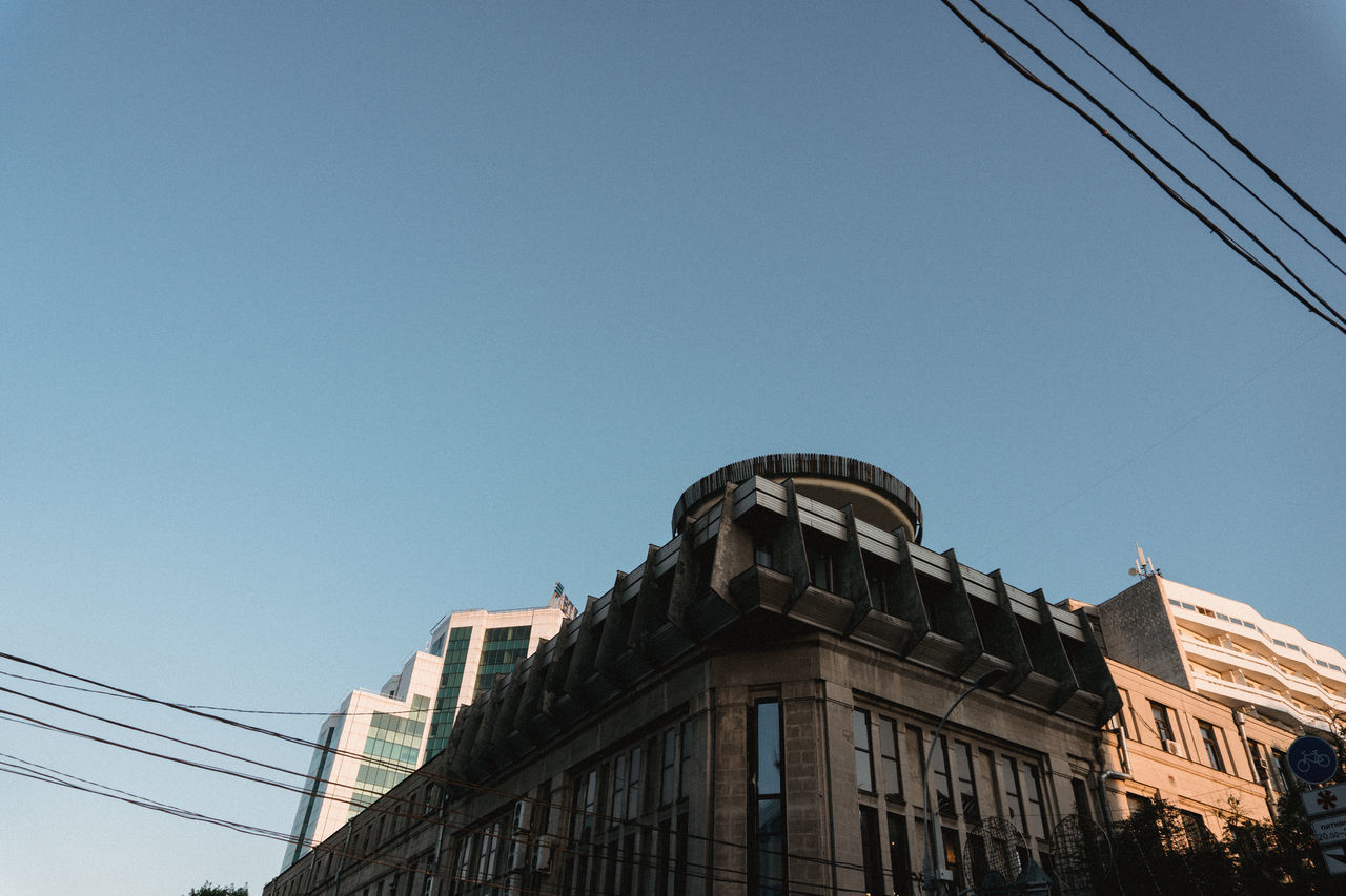 built structure, sky, architecture, low angle view, building exterior, clear sky, copy space, nature, day, building, blue, no people, cable, city, outdoors, connection, window, sunlight, construction industry, power line, power supply