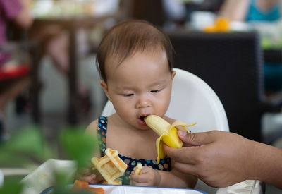 Cropped hand of mother feeding banana to daughter in restaurant