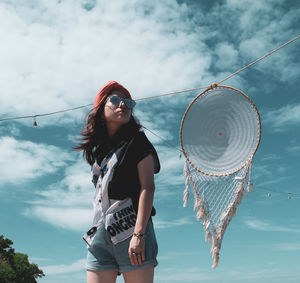 Young woman wearing sunglasses standing against sky