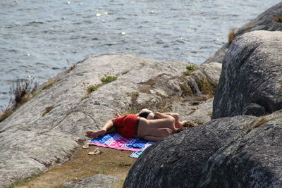 Low section of woman sitting on rock by sea