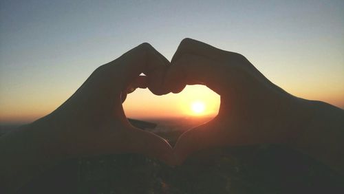 Close-up of hand touching heart shape against sky during sunset