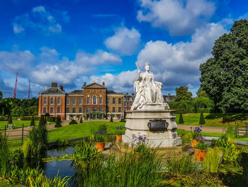 Statue in front of building against cloudy sky