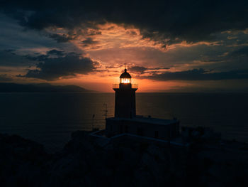 Lighthouse by sea against sky during sunset