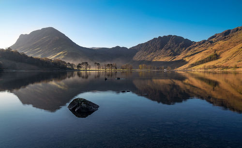 Scenic view of lake and mountains against clear blue sky