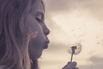 Close-up of young woman holding dandelion against white wall