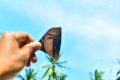 Close-up of hand holding plant against blue sky