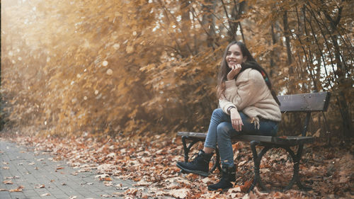 Young woman sitting on bench in park during autumn