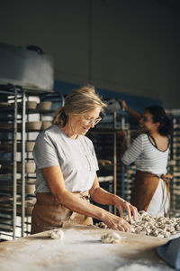 Smiling senior female baker arranging cinnamon buns on tray while working at bakery