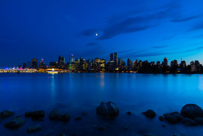 Illuminated city by sea against sky at dusk