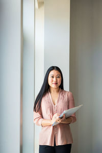 Portrait of confident businesswoman with file standing against wall in office