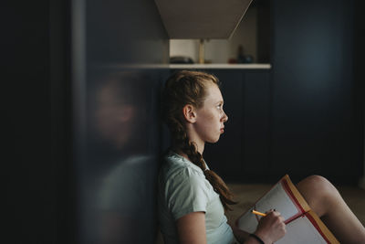 Thoughtful girl sitting on floor while studying at home