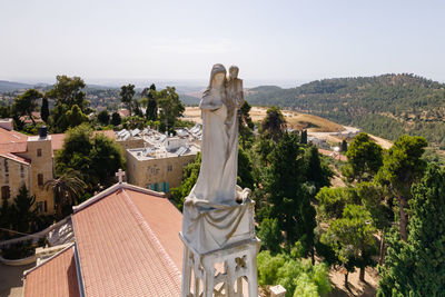 Statue amidst trees and buildings against sky