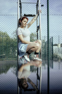 Portrait of woman sitting by chainlink fence