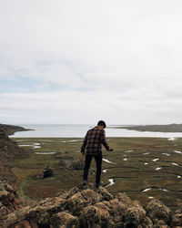 Man standing on rock looking at sea against sky