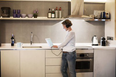 Side view of mature woman using laptop at kitchen counter