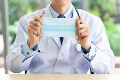 Midsection of doctor holding mask in hospital