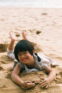 Portrait of smiling girl lying on sand at beach