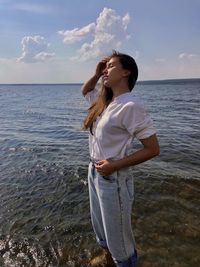 Young woman standing at beach against sky