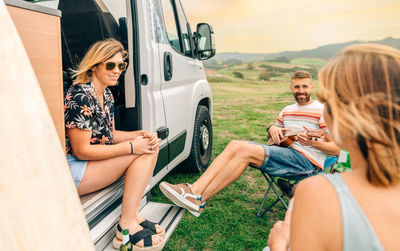 Friends having fun talking and playing ukulele in front of their camper van