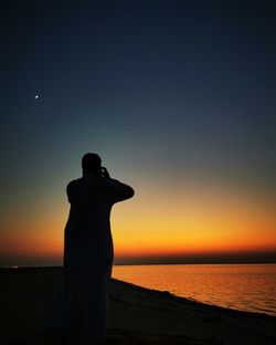 Silhouette man looking at sea against sky during sunset