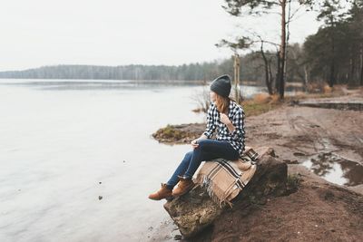 Woman sitting by lake against sky