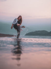 Woman in sea against sky during sunset