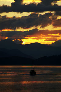 Silhouette sailboat on sea against orange sky