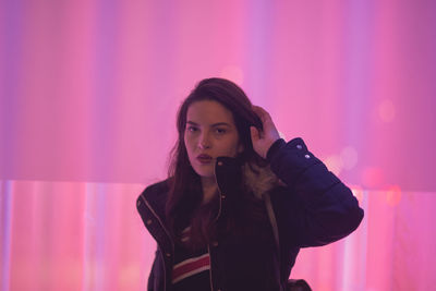 Portrait of young woman standing against pink light at night