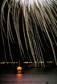 Illuminated suspension bridge over river against sky at night