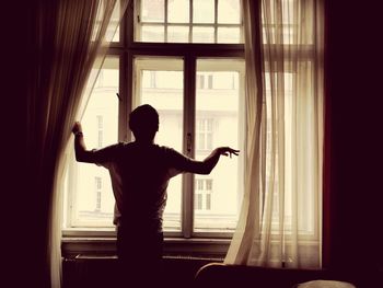 Rear view of man standing by window at home