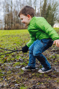 A young boy in winter clothes plays with a stick in the mud