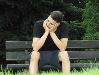 Sad young man sitting on bench at park