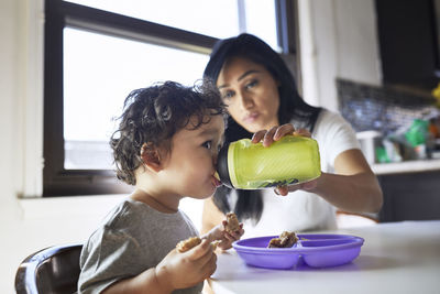 Mother feeding water to son from bottle at home