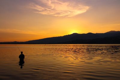Silhouette person on lake against sky during sunset