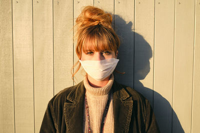 Portrait of woman wearing mask standing against wall