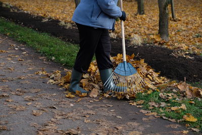 Low section of man raking leaves on street during autumn