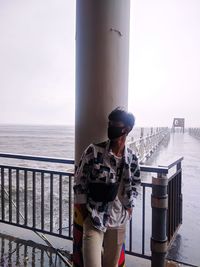 Man standing wearing mask standing by railing against sea