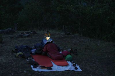 Woman writing on book while camping on field at dusk