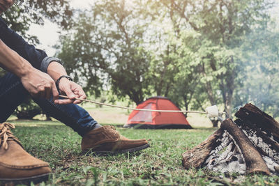 Low section of man roasting marshmallow in campfire