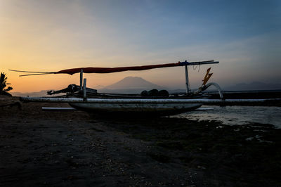 Fishing boat on beach against sky during sunset