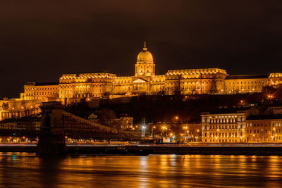 Illuminated buda castle at night above the danube river in budapest, hungary