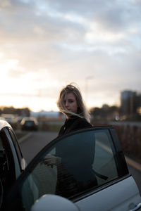 Portrait of young woman standing against car