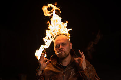 Portrait of man with flame on head smoking against black background