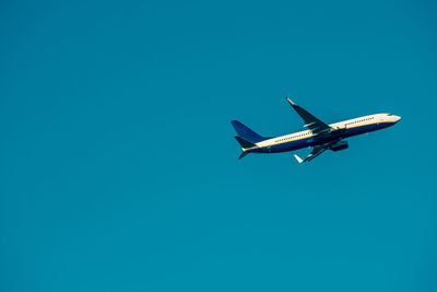 Low angle view of airplane flying against clear blue sky