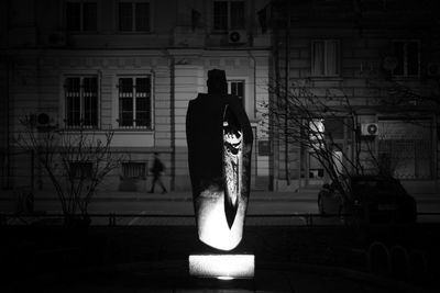 Man standing by illuminated street against building at night